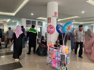 Di sela keramaian koridor kantin, seorang pedagang asongan terlihat sabar menanti pembeli di tengah lalu-lalang para wisudawan dan keluarga yang merayakan kelulusan. Sabtu, 08/08/2026.