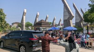 Terlihat petugas keamanan merentangkan tangan untuk mengatur kelancaran arus kendaraan dan pejalan kaki di depan gerbang kampus saat momentum wisuda. Sabtu, 08/08/2026.